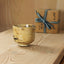 Ceramic cup on a wooden surface with a wrapped gift box in the background