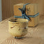 Ceramic cup with crane engraved and black brush patterns on a wooden surface, next to a wooden box with a blue ribbon.